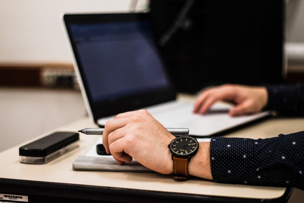 A man experiencing wrist and finger pain while sitting at a desk with a laptop and a watch.