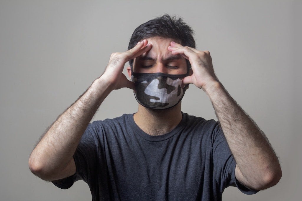 A man with a face mask experiencing migrane headaches.