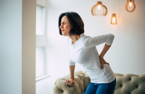 A woman experiencing back pain from standing seeks relief while sitting on a couch.