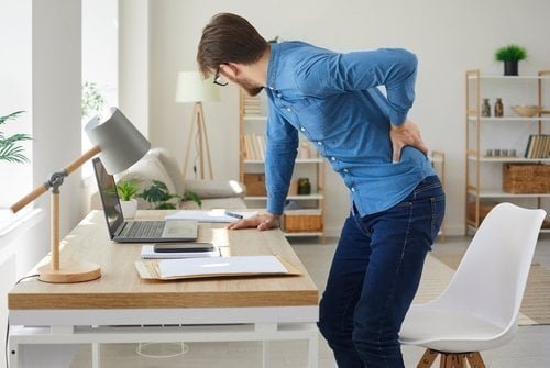 A man is sitting at his desk with his Spondylolisthesis pain.