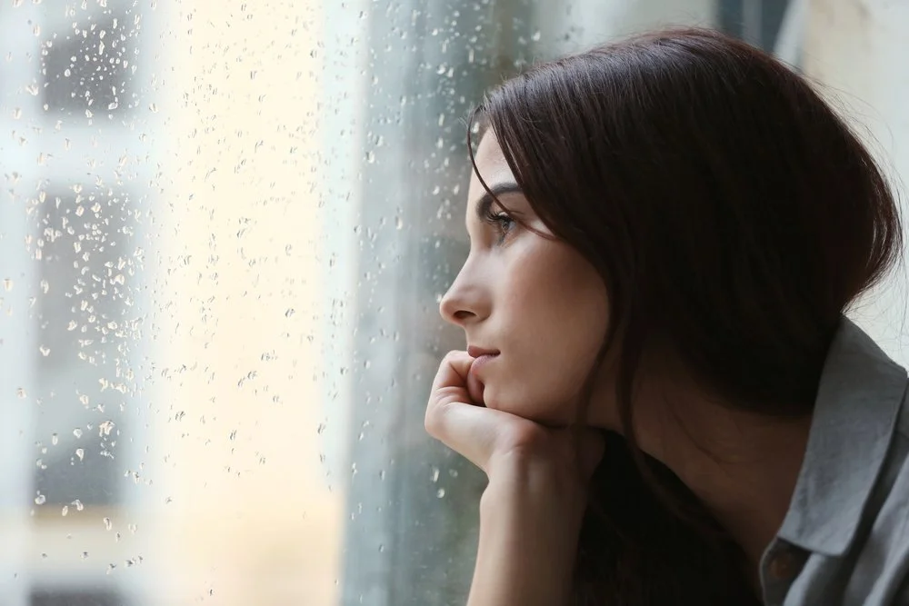 A woman looking out of a window with raindrops on her face.