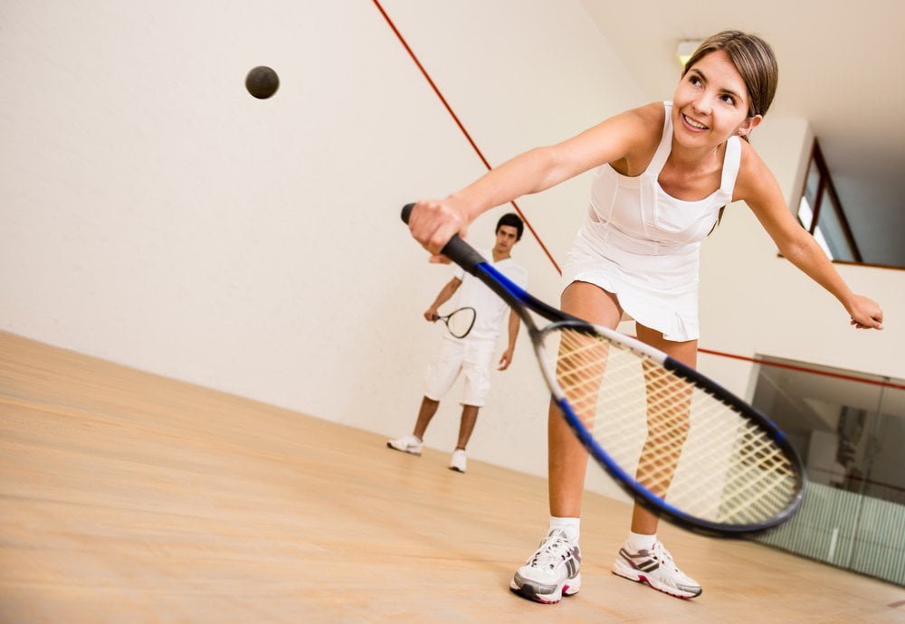 A woman is playing squash at a sports injury clinic with a racket.