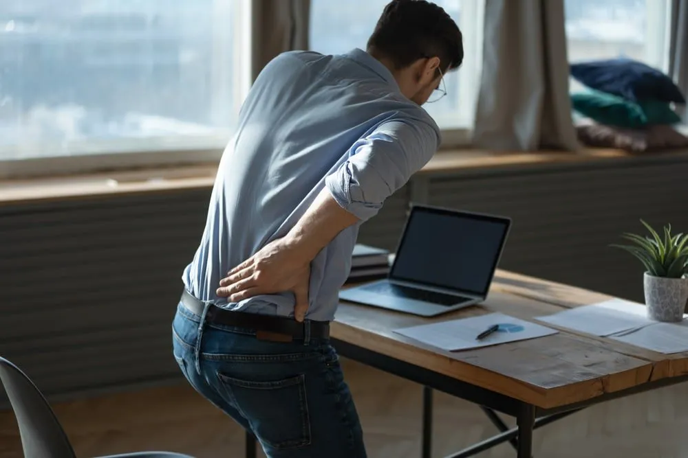 A man in London is sitting at a desk with his back hurting, seeking relief from an osteopath.