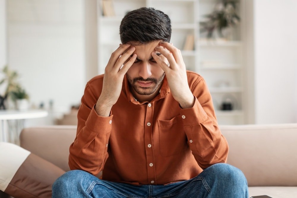 A man sitting on the couch with his hands on his head.