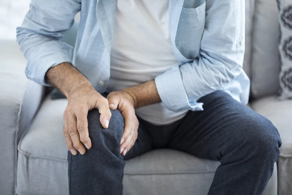 A man sitting on a couch in London with his knee hurting.