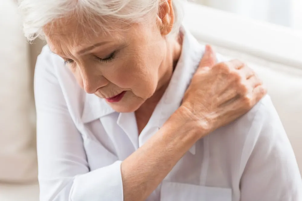 A woman in London with a shoulder pain is sitting on a couch.