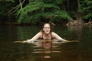 A woman with closed eyes treading water in a calm Hamstead Heath lake, keeping fit.