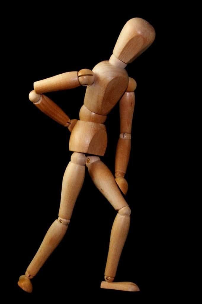 Wooden artist's mannequin posed walking against a black background, mimicking sciatica.